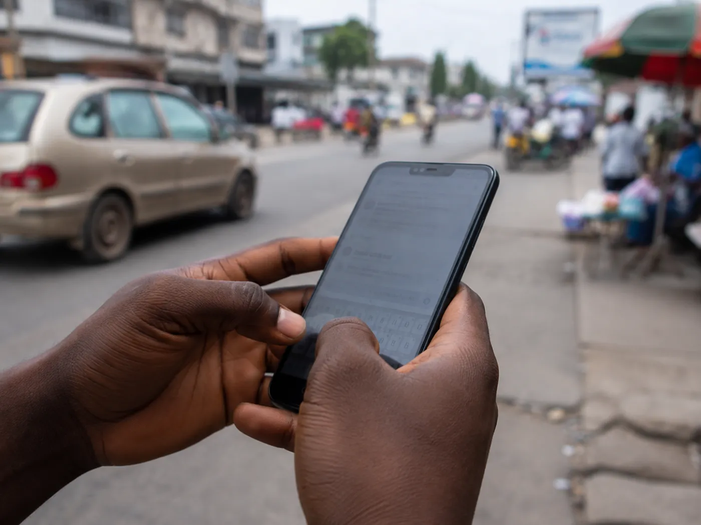 Gros plan sur les mains d'une personne qui saisit une commande sur son téléphone, dans une rue de Cotonou.