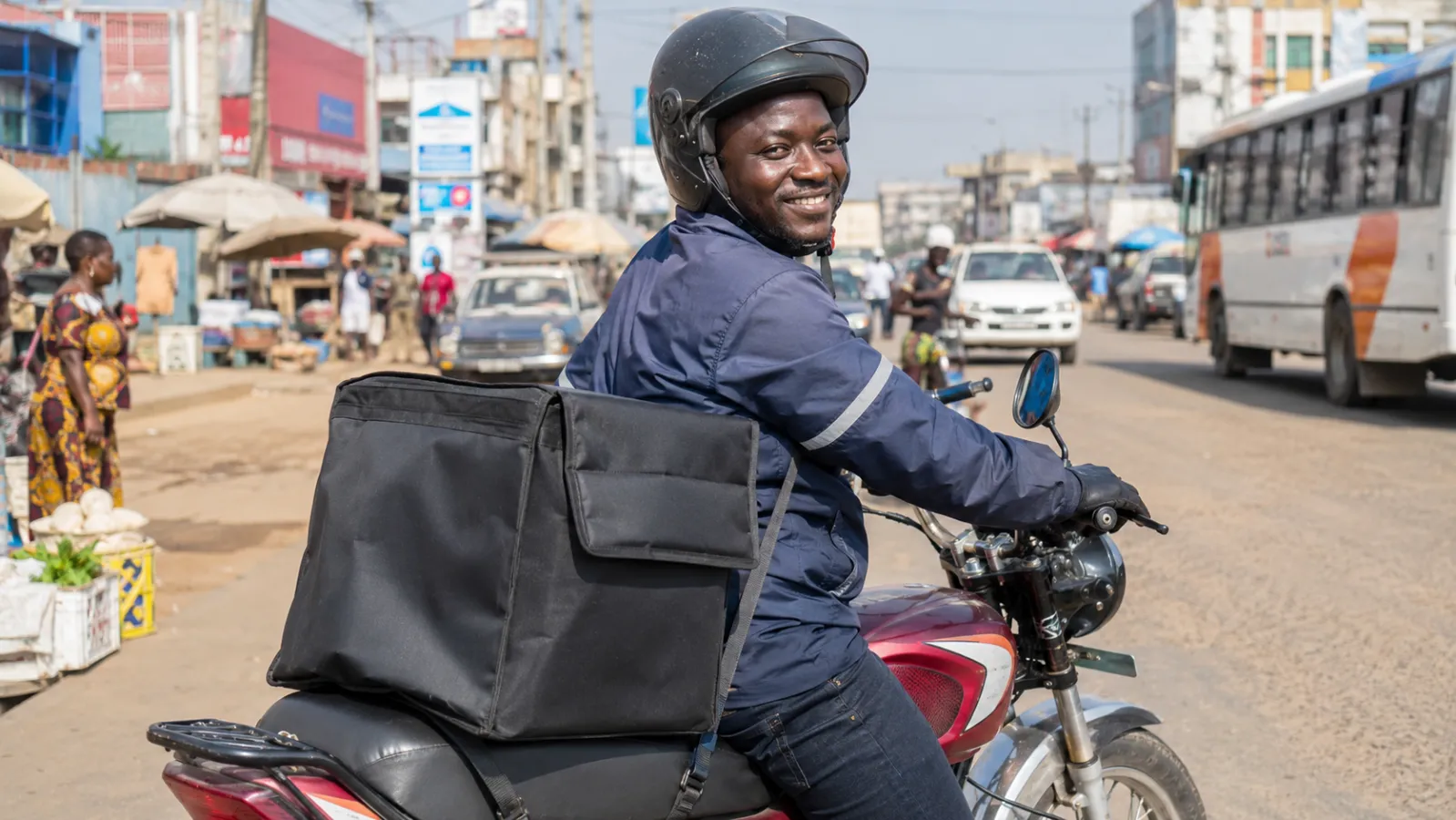 Un livreur béninois à moto, sacoche de livraison à l'arrière, dans une rue de Cotonou.